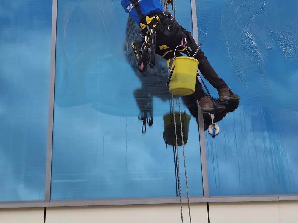 Técnico de mantenimiento trabajando en la fachada de un edificio con cuerdas y arnés